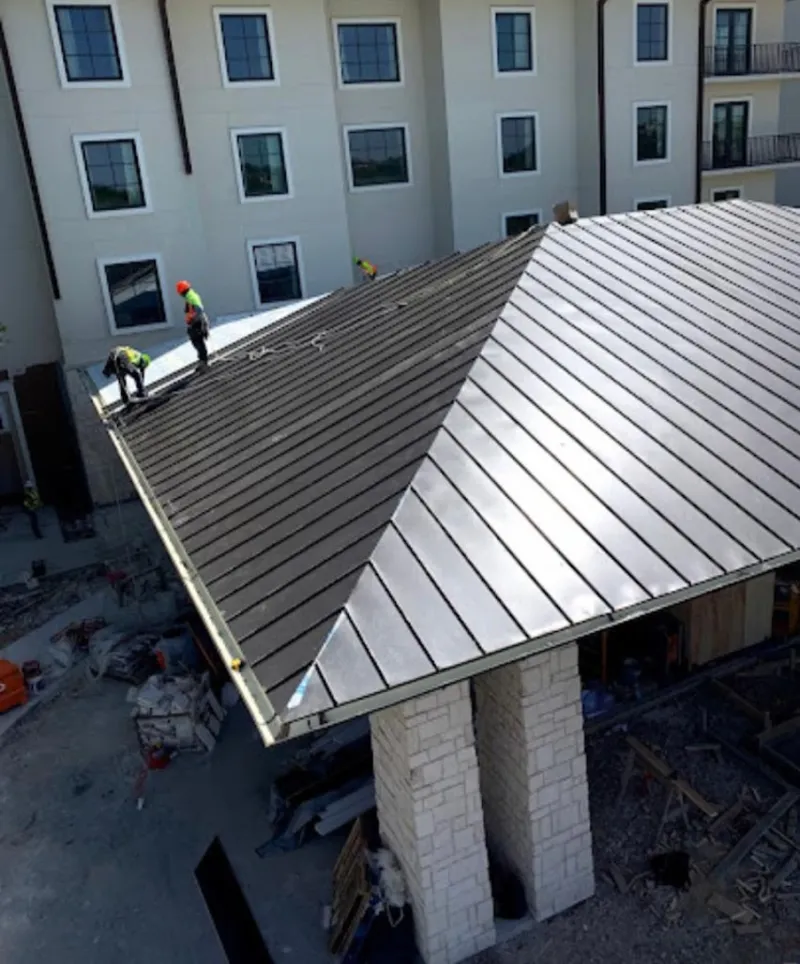Crew installing standing seam metal roof panels on a commercial project in Kenton